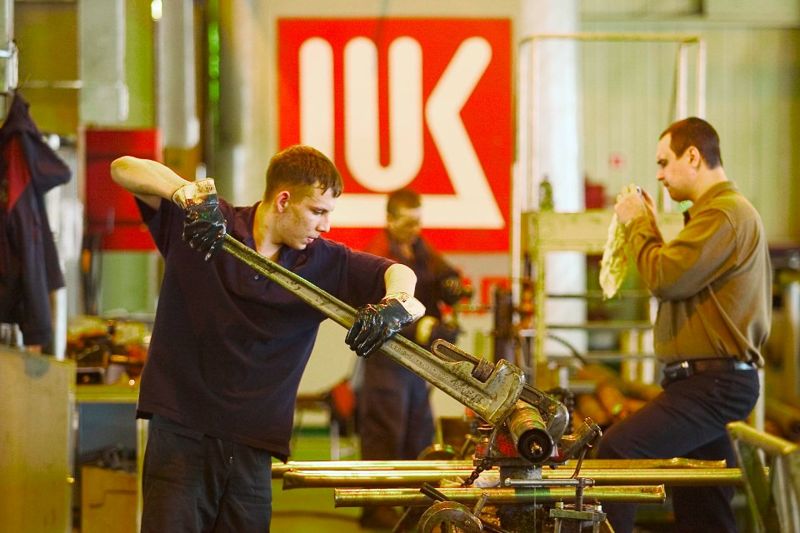 Рабочий работает на станке на фоне логотипа "Лукойла"