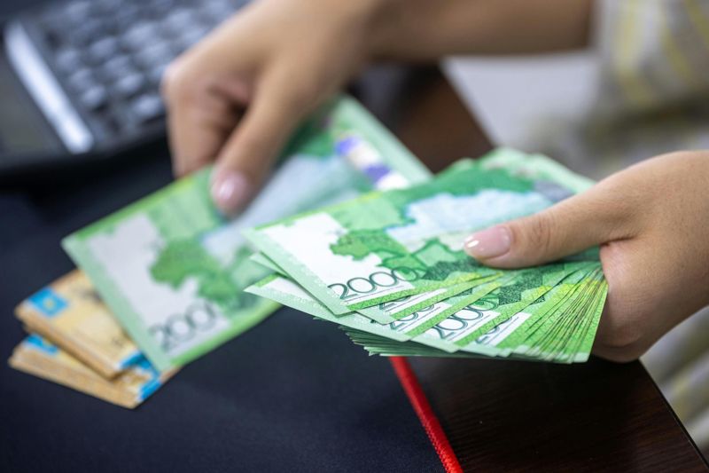 Национальная валюта тенге, руки держат тенге