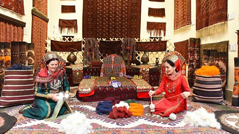 Женщины туркменки на фоне ковров прядут шерсть