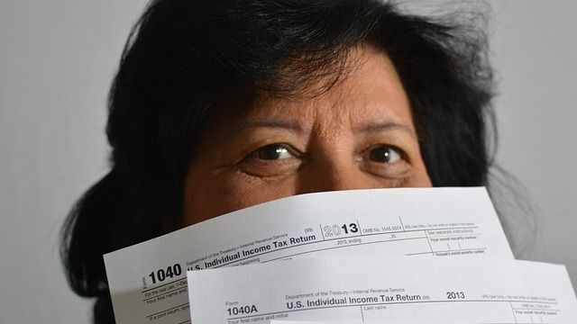 Женщина закрывает лицо налоговыми декларациями, налоги, упрощенка, СНР, самозанятые